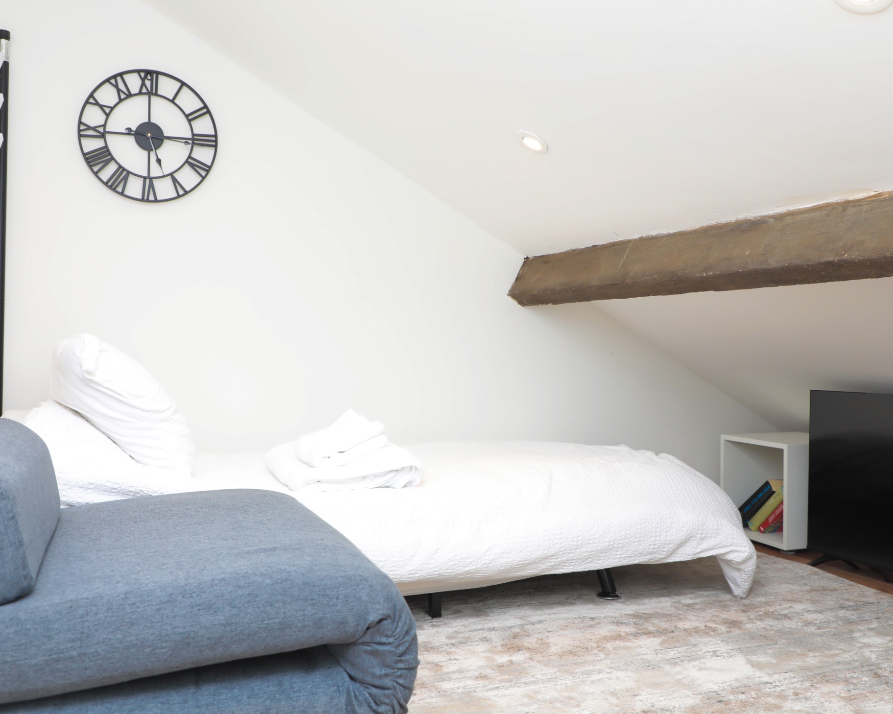 Loft sleeping area with a grey sofa and original timber beam